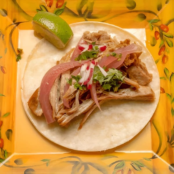 A Mis Taquitos carnitas taco with pickled red onions, radishes, cilantro, and a lime wedge.