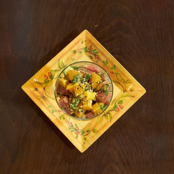 Mis Taquitos' ceviche with tuna, mango, and sesame seeds in a glass bowl on a decorative plate.
