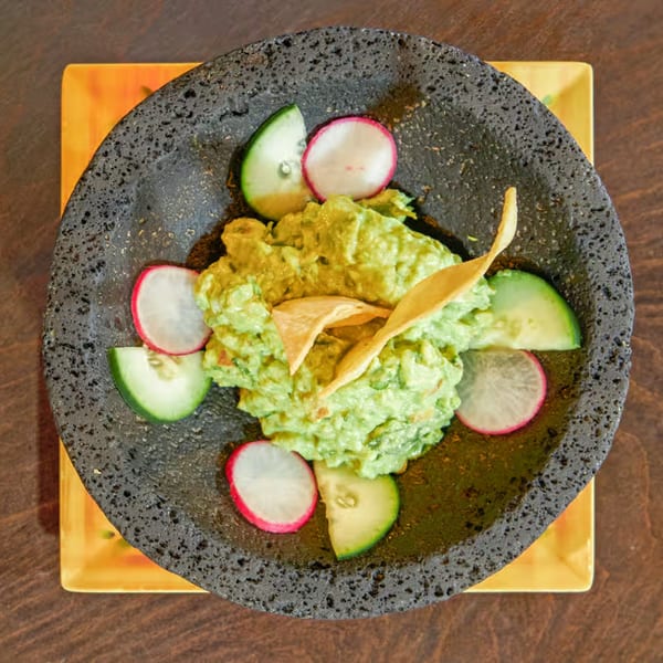 Fresh guacamole with tortilla chips, cucumber, and radish slices in a dark stone bowl.