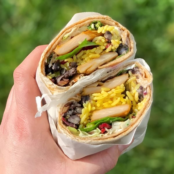Hand holding a Mis Taquitos burrito, cut in half, revealing chicken, yellow rice, and black beans.