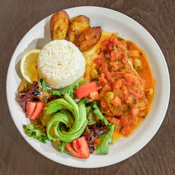 A Mexican dish with fish in tomato sauce, rice, fried plantains, and a fresh salad.